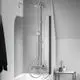 Duschsystem mit Kopf- und Handbrause in Chrom, montiert an der Wand. Badarmatur von Ideal Standard, neben einem weißen Badebereich und einem kleinen Beistelltisch.